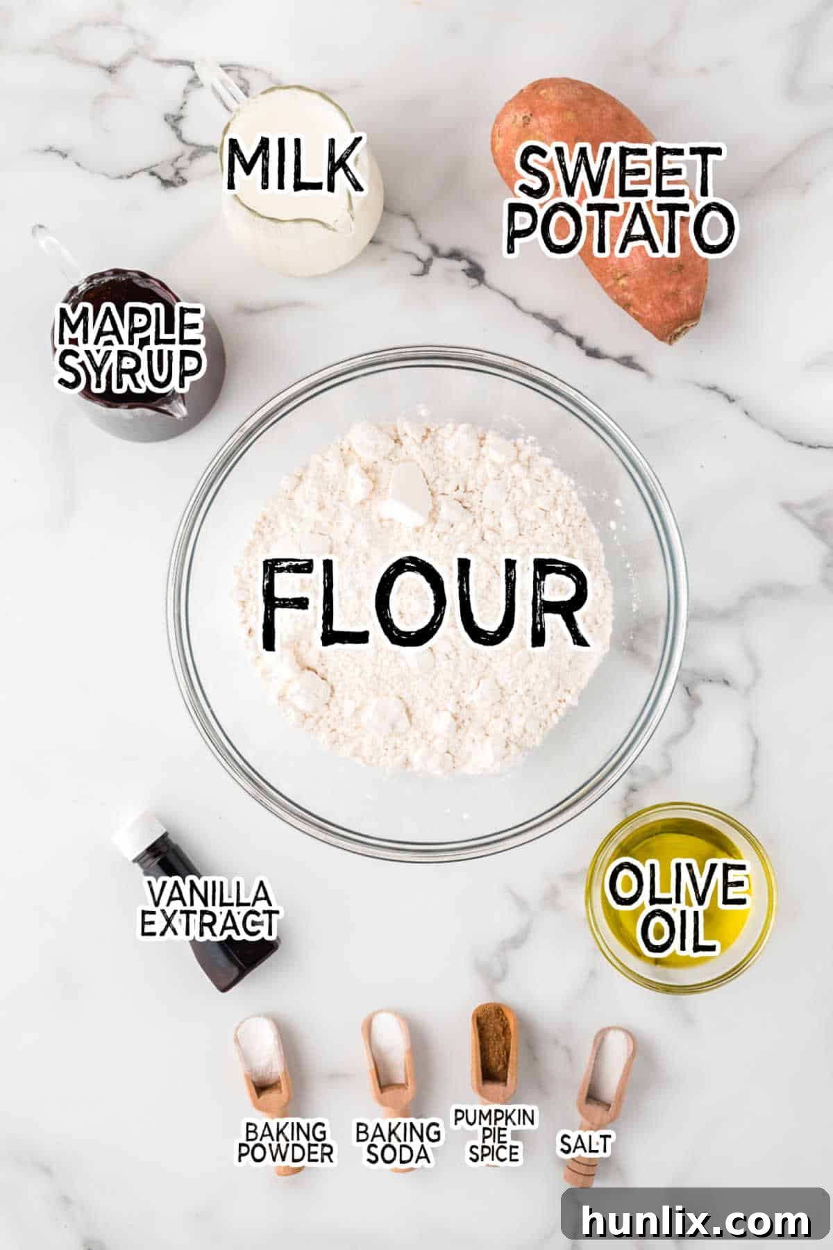 A vibrant display of fresh ingredients for sweet potato muffins, including a roasted sweet potato, maple syrup, flour, and spices, arranged on a marble counter.