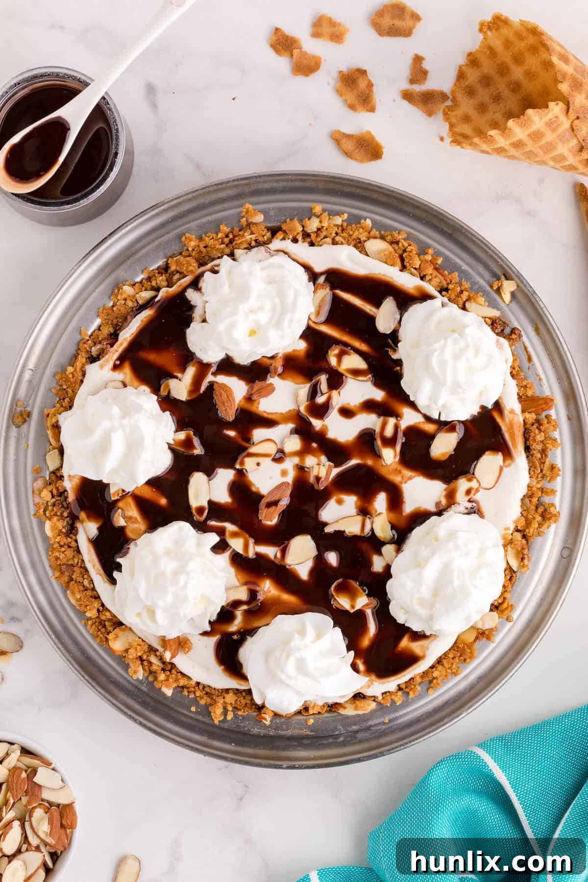 A beautifully crafted ice cream pie in a pie pan, ready to be sliced, showcasing layers of waffle cone crust, chocolate, and vanilla ice cream with a drizzle of syrup.