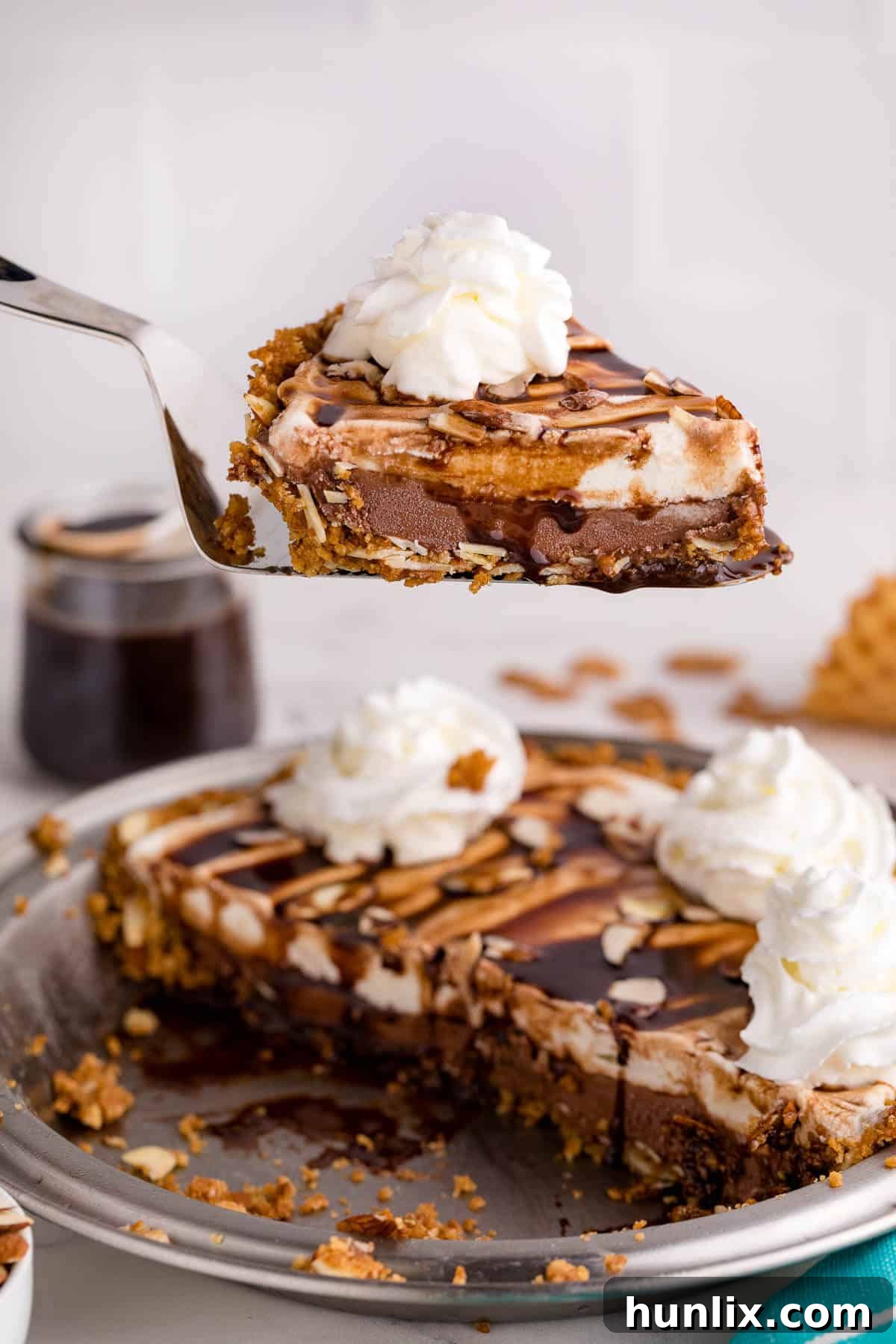 A slice of ice cream pie perfectly positioned on a pie server, showcasing its distinct layers of crust, chocolate, and vanilla ice cream, with a luscious chocolate drizzle on top.