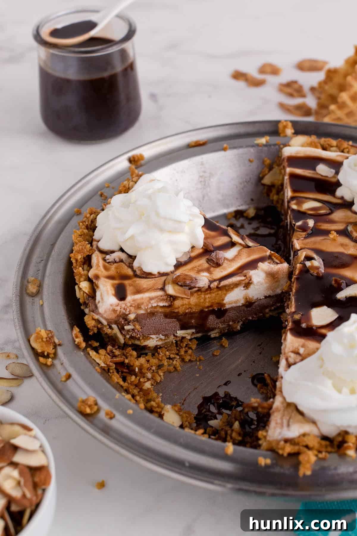 A whole ice cream pie in a pie pan, already sliced into generous portions, showing the beautiful layers of crust, chocolate, and vanilla ice cream, topped with chocolate drizzle.