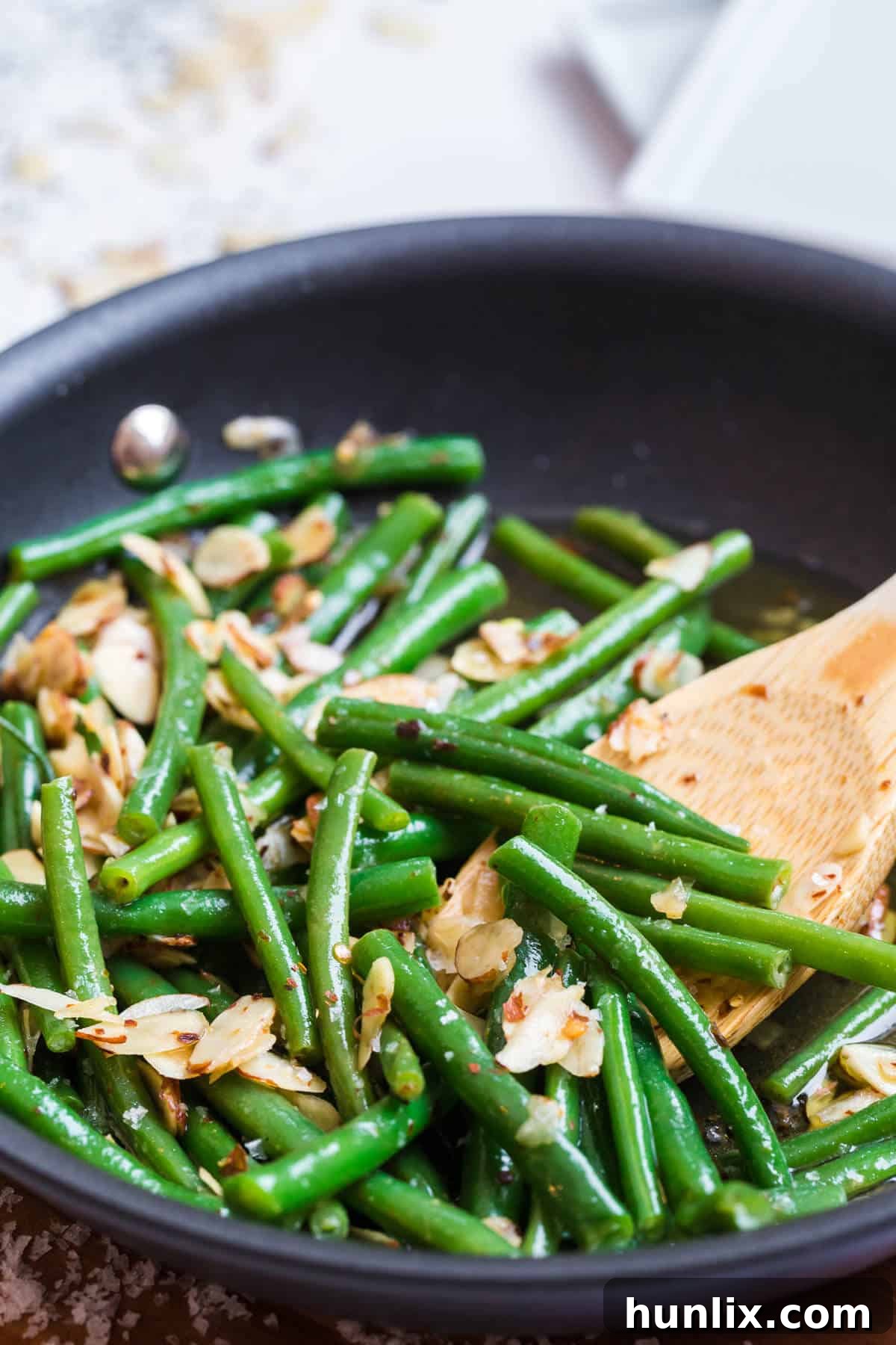 Buttery Chili Green Beans with Toasted Almonds 4 A wooden spoon stirs perfectly cooked chili buttered green beans and almonds in a black skillet.