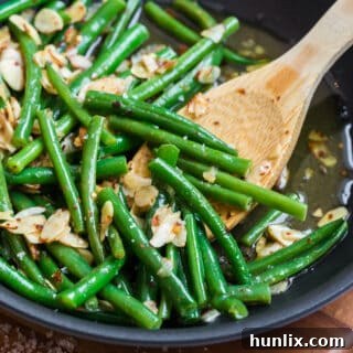 Chili buttered green beans in a skillet with a wooden spoon.