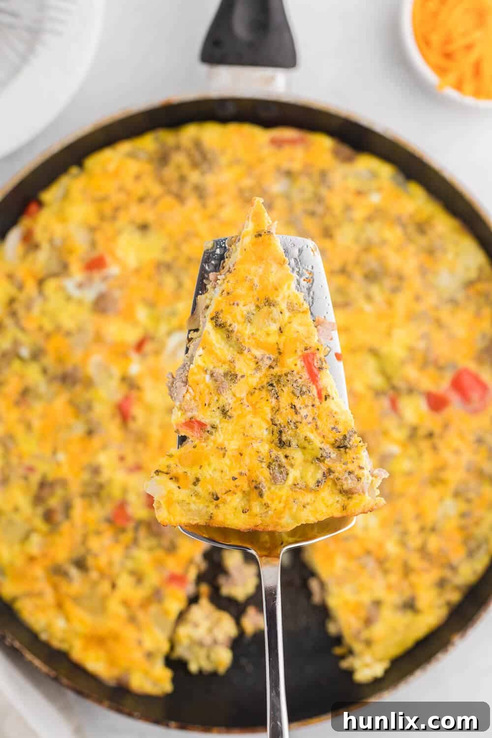 A whole Sausage & Red Pepper Frittata in an oven-safe skillet, garnished with fresh herbs, ready to be sliced and served for a family meal.