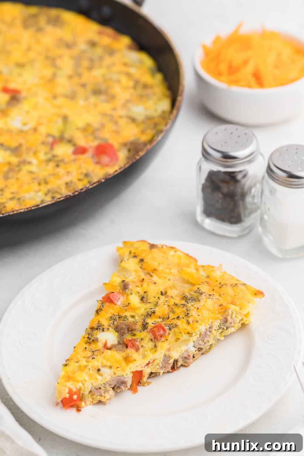 Fresh ingredients laid out for Sausage & Red Pepper Frittata, including eggs, sausage, chopped red peppers, and onions, on a wooden cutting board.