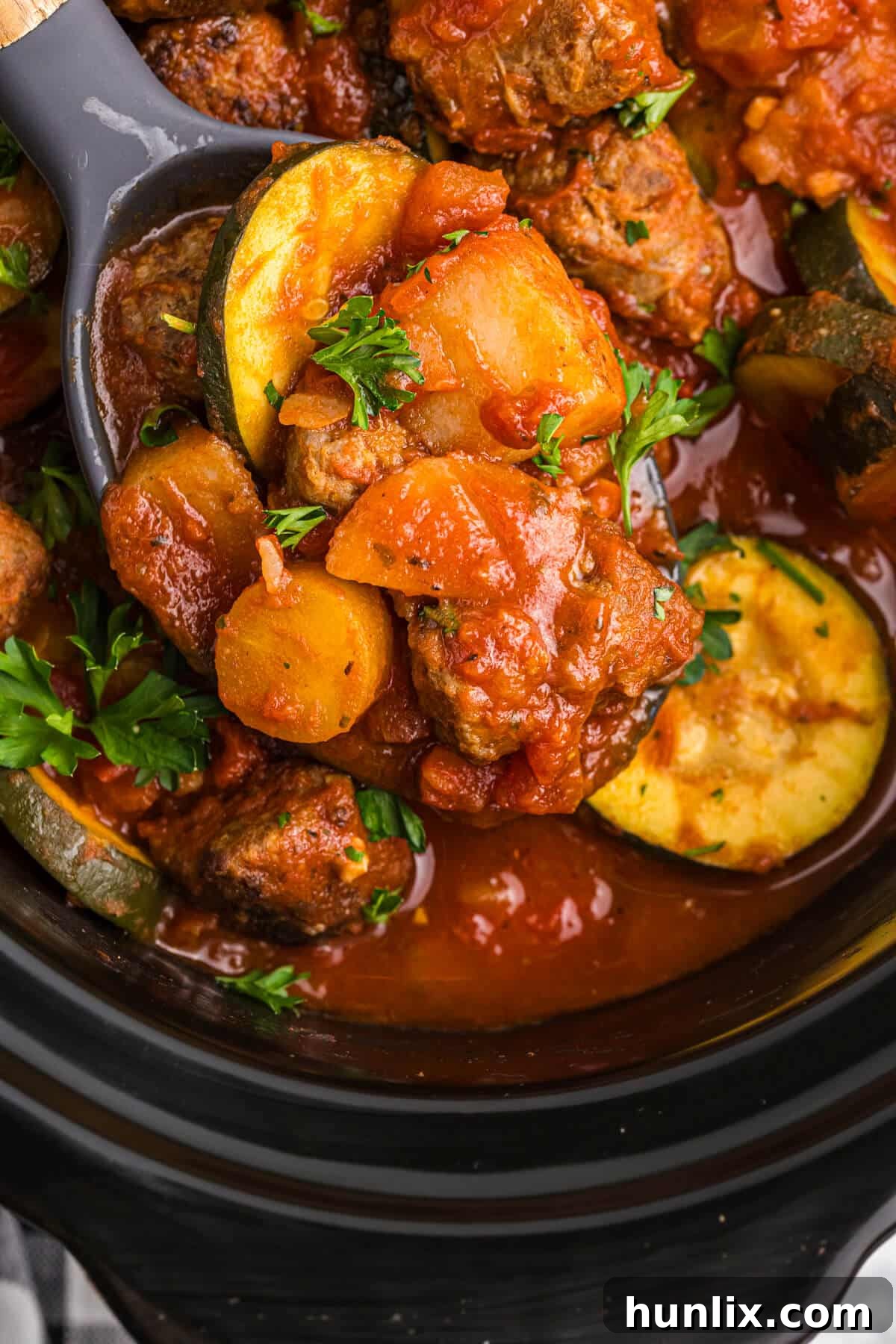 Italian sausage and vegetable stew with a serving spoon in a Crockpot.