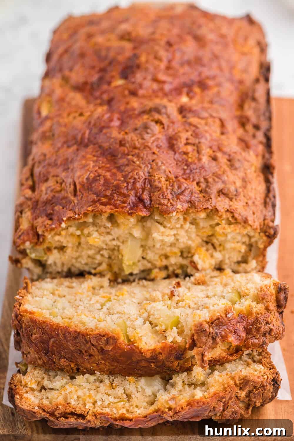 Tangy Cheddar and Sweet Apple Quick Bread 3 A loaf of freshly baked Apple Cheddar Quick Bread with several slices already cut, revealing the tender crumb filled with apple pieces and melted cheese.