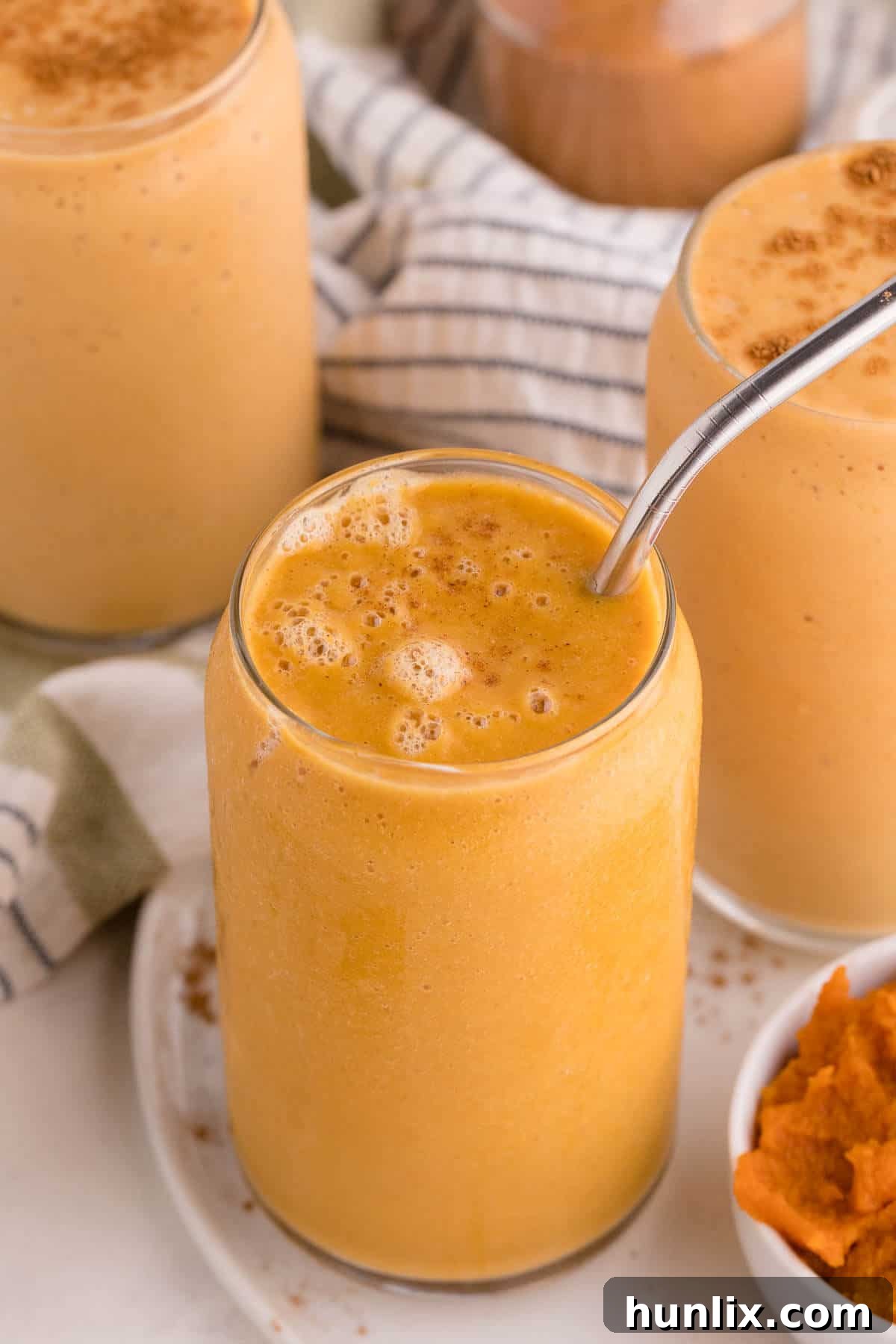 Velvet Pumpkin Sip 2 Creamy Pumpkin Pie Smoothie served in a clear glass with a metal straw, garnished with a sprinkle of pumpkin pie spice.