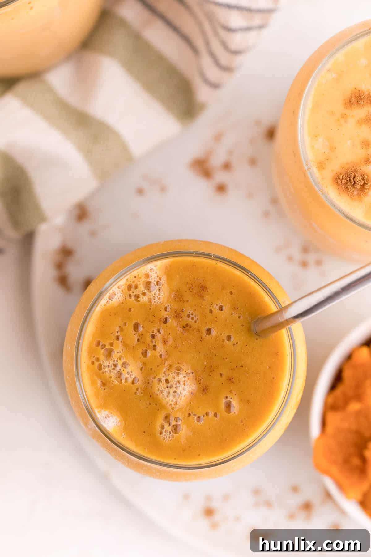 Velvet Pumpkin Sip 6 Overhead view of a single pumpkin pie smoothie in a glass with a metal straw, highlighting its creamy texture.