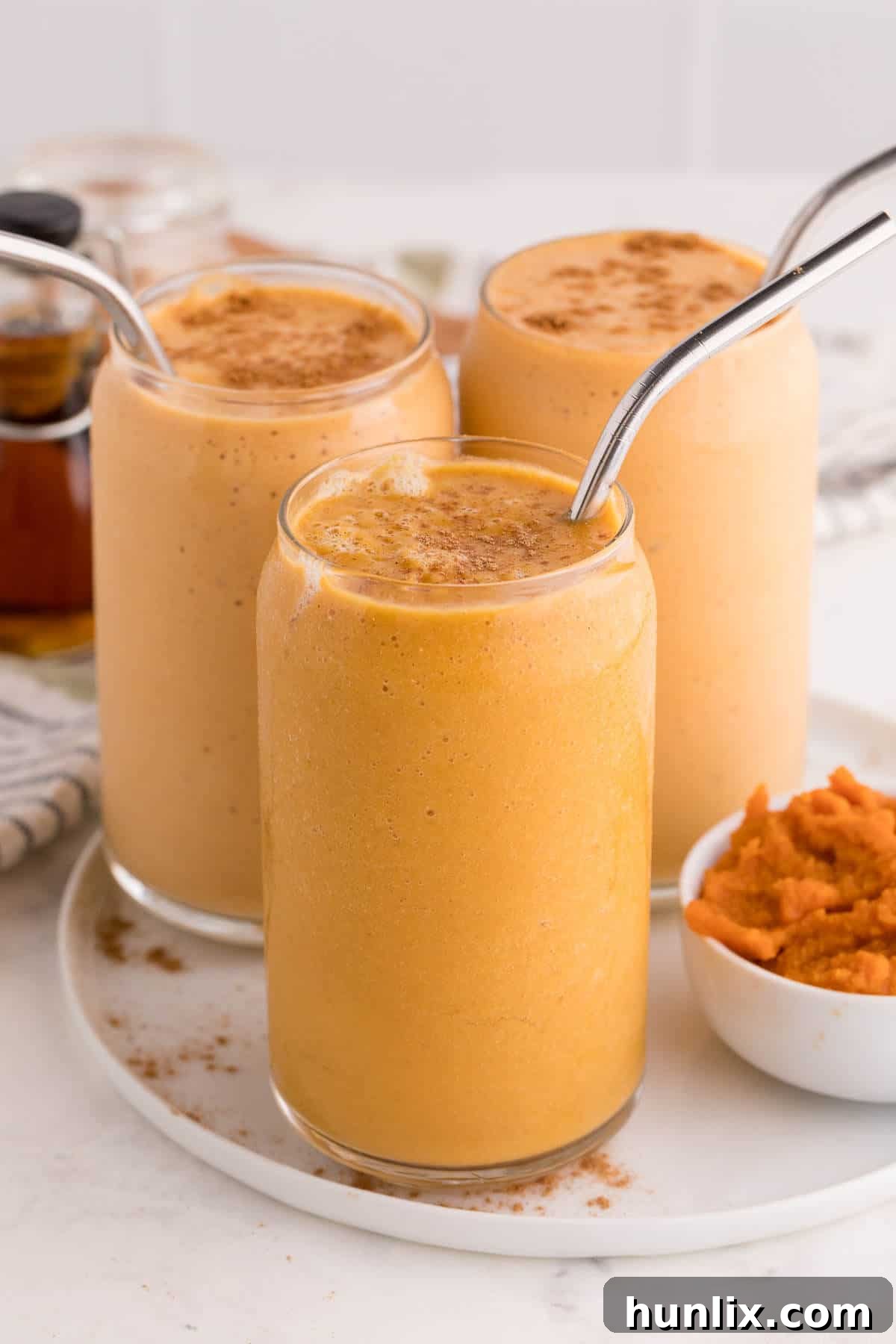 Velvet Pumpkin Sip 7 Three pumpkin pie smoothies artfully arranged on a white plate, ready to be served.