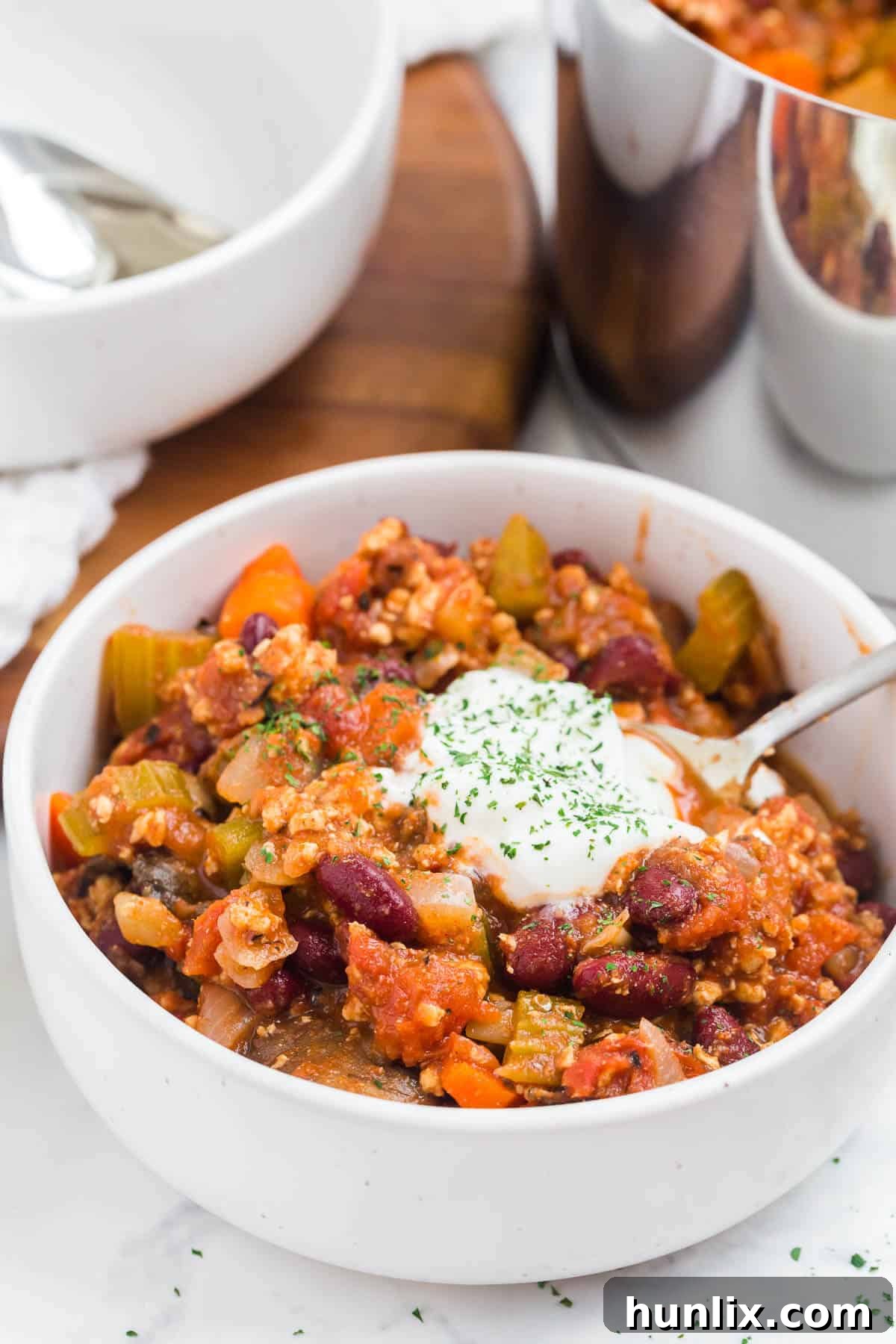 A hearty bowl of chicken chili, garnished with cheese and sour cream, with a spoon resting in it.