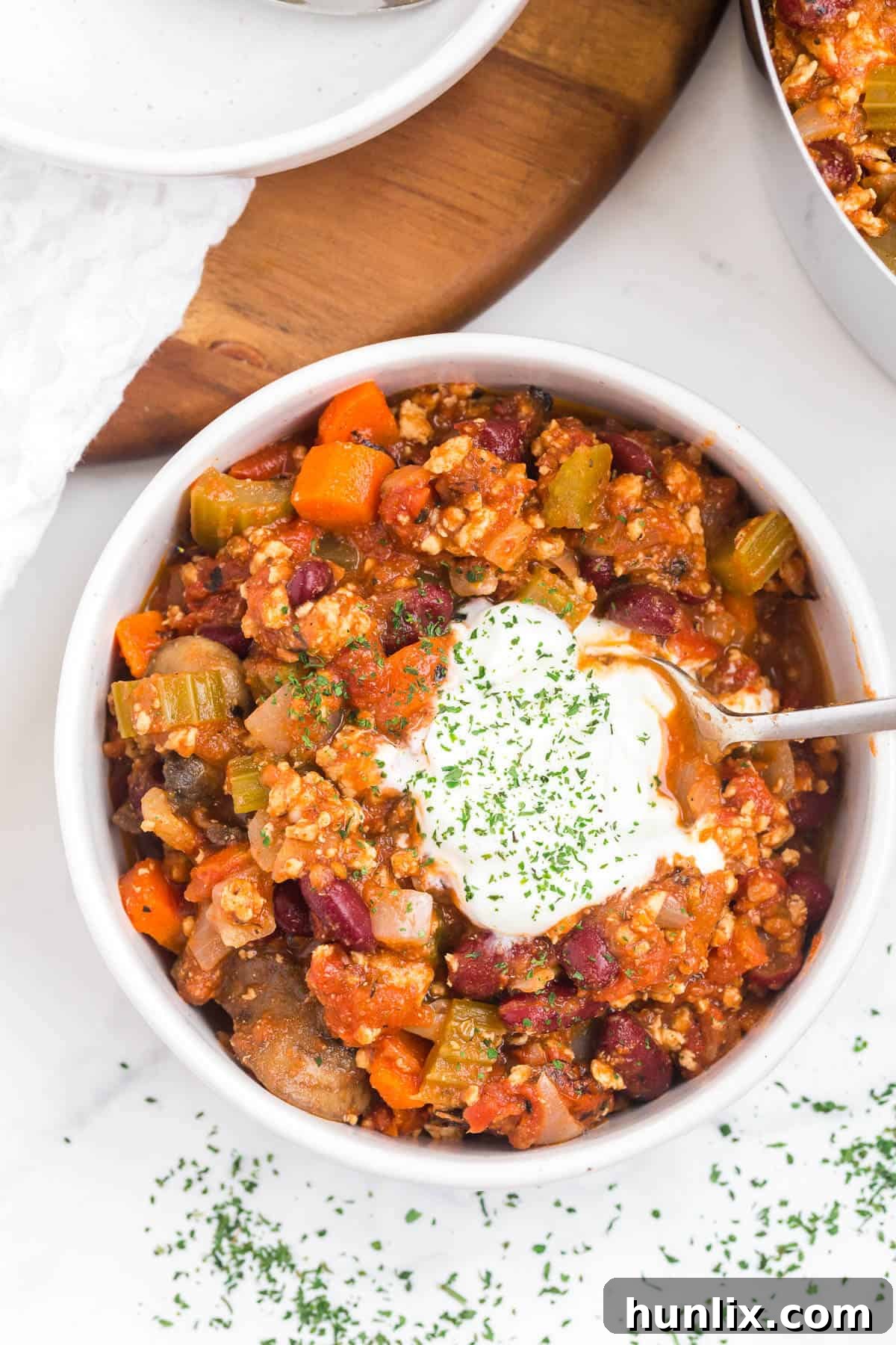 A delightful bowl of chicken chili, generously topped with sour cream, shredded cheese, and fresh cilantro, with a spoon nearby.