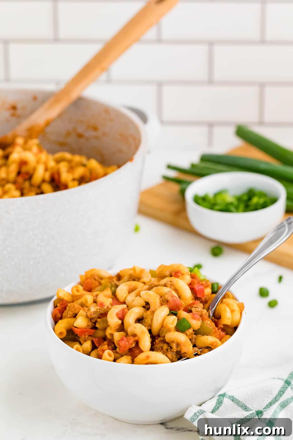 A white bowl and spoon with beef taco pasta, garnished with fresh herbs.