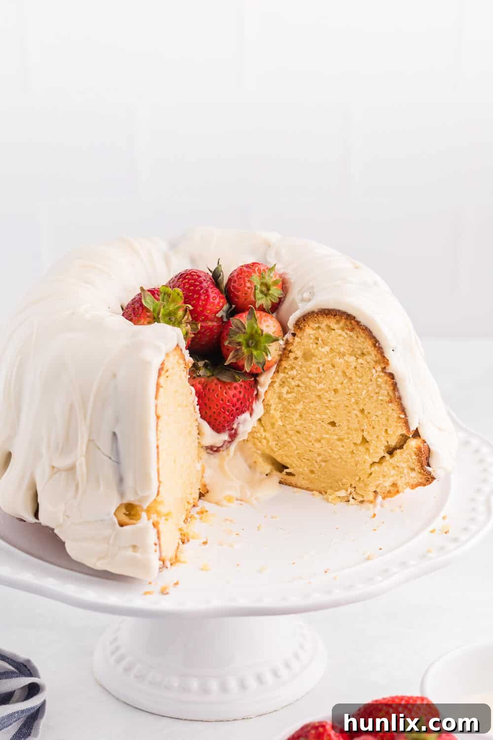 A large Vanilla Cream Cheese Cake on a cake stand, with several slices already cut, revealing the moist interior.