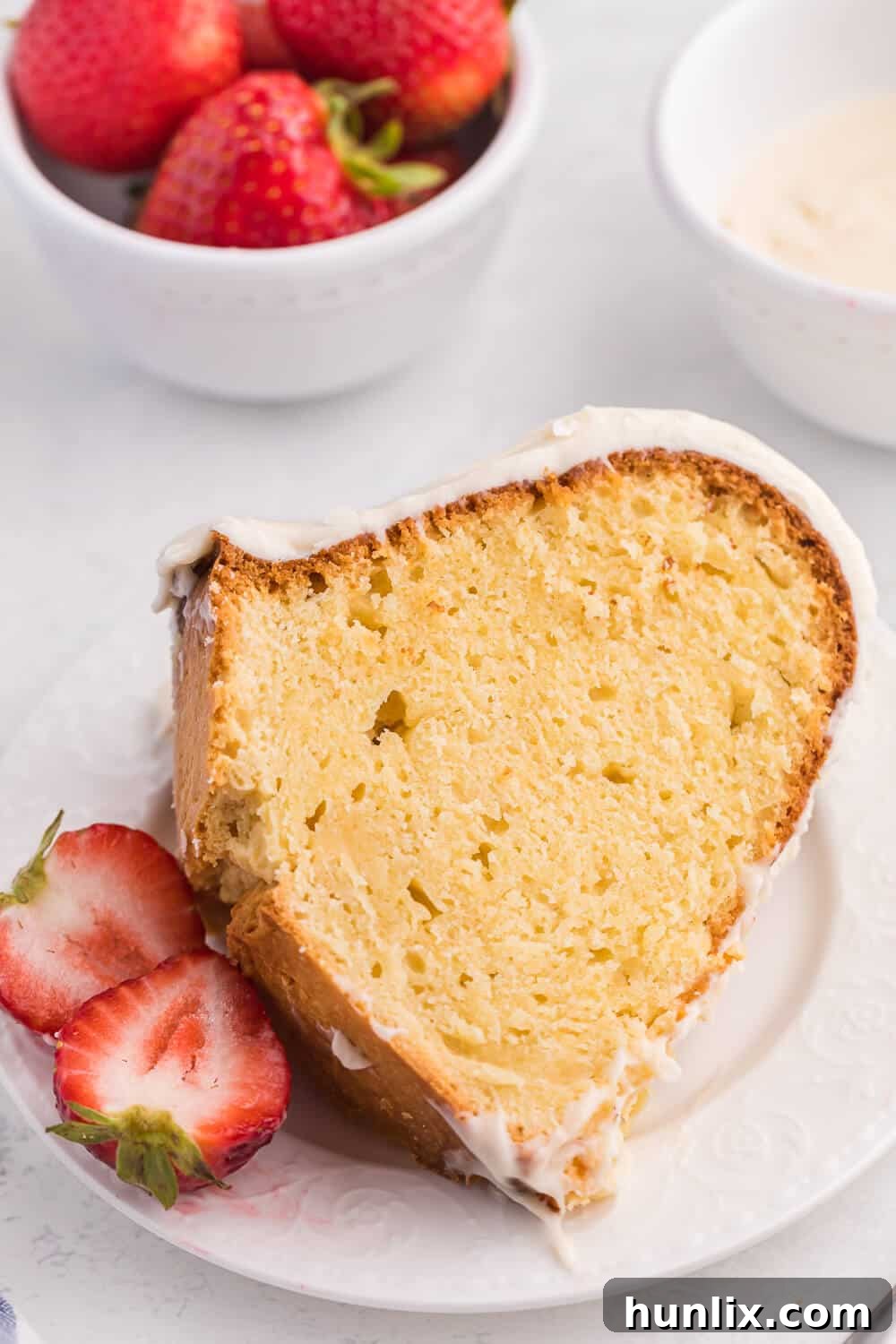 A slice of Vanilla Cream Cheese Cake on a white plate, garnished with fresh strawberries.
