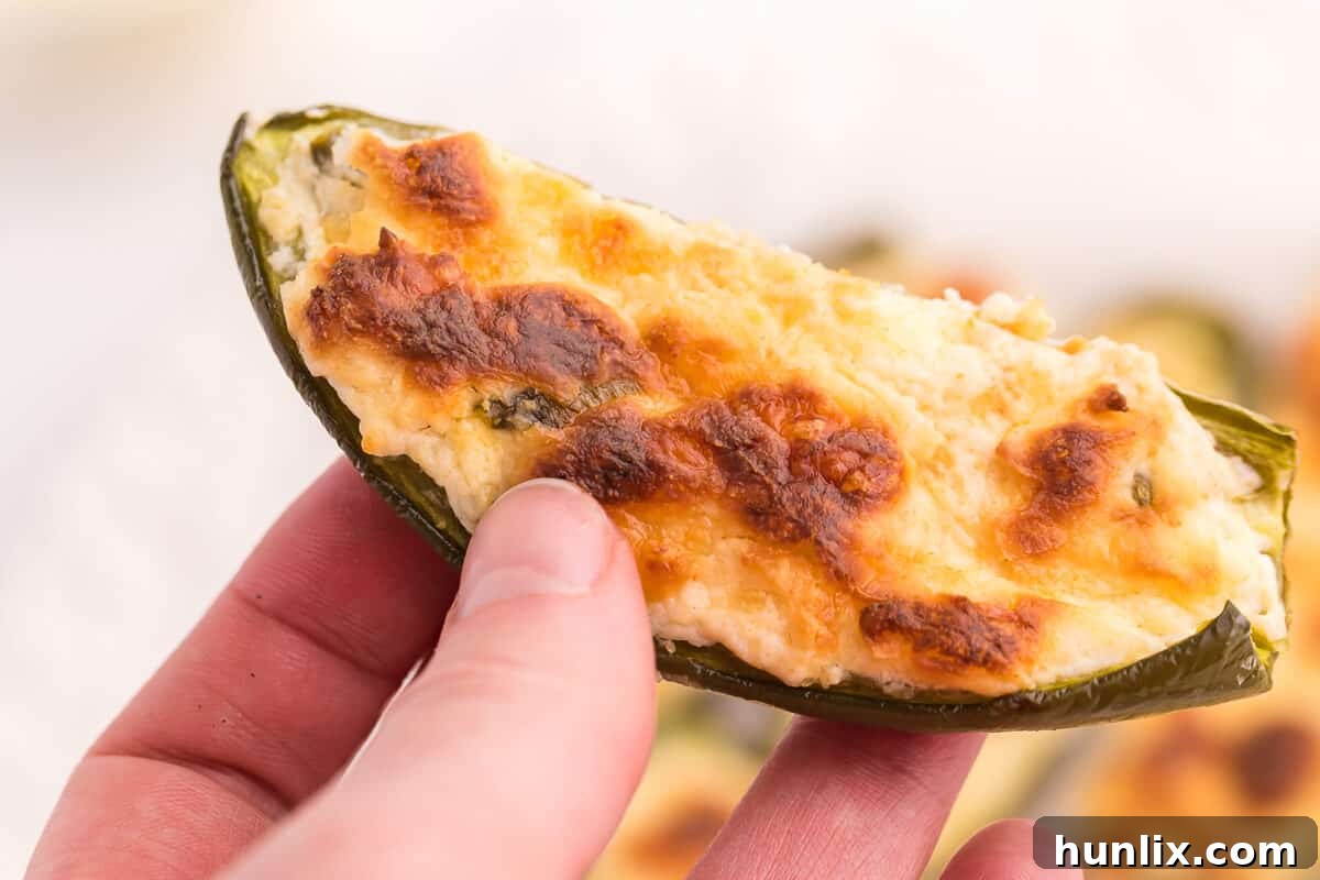 A hand holding a freshly baked, golden-brown cream cheese stuffed jalapeno, showing its inviting filling.