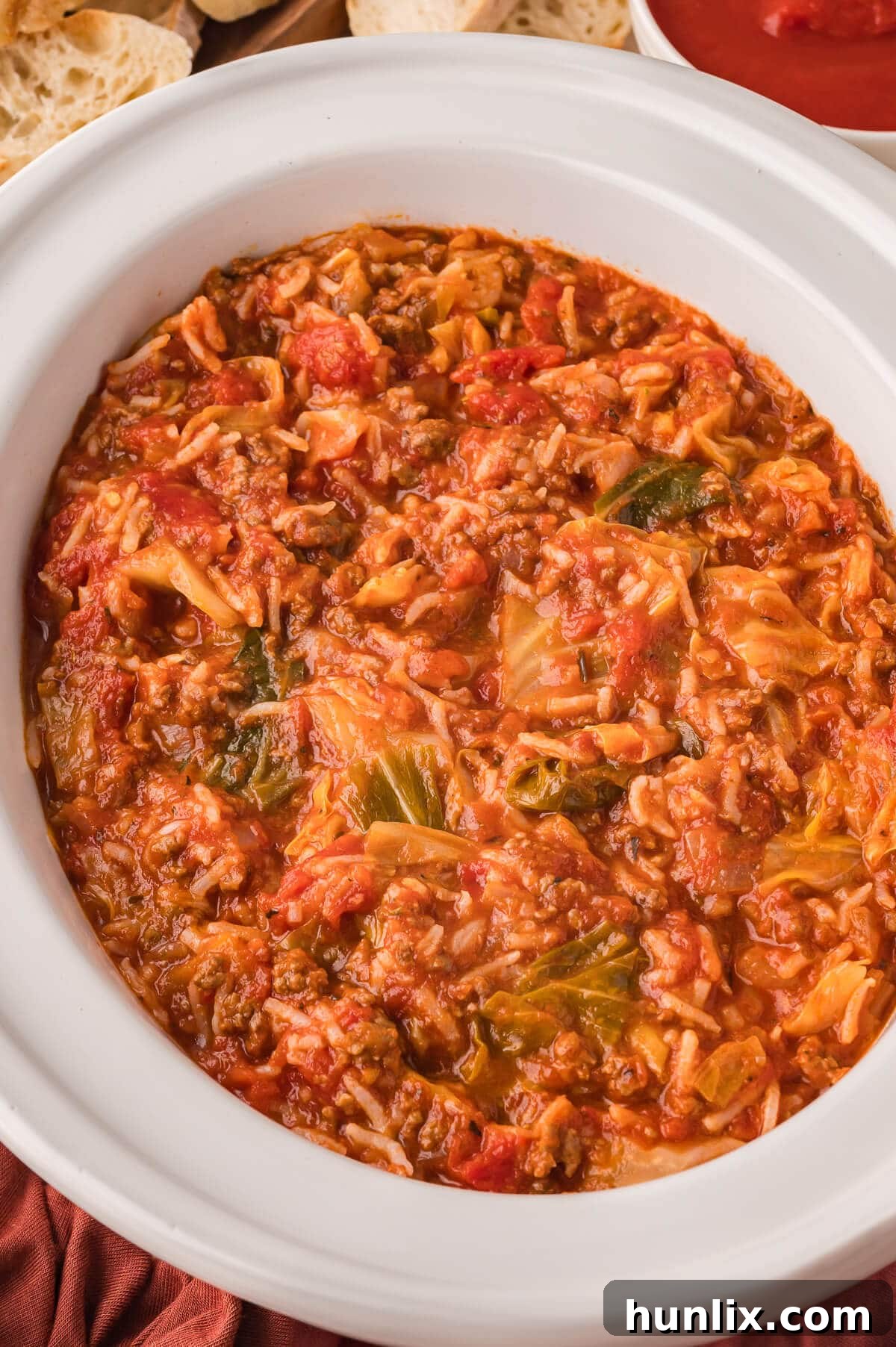 A white slow cooker filled with steaming Cabbage Roll Soup, garnished with fresh herbs, ready to be served.