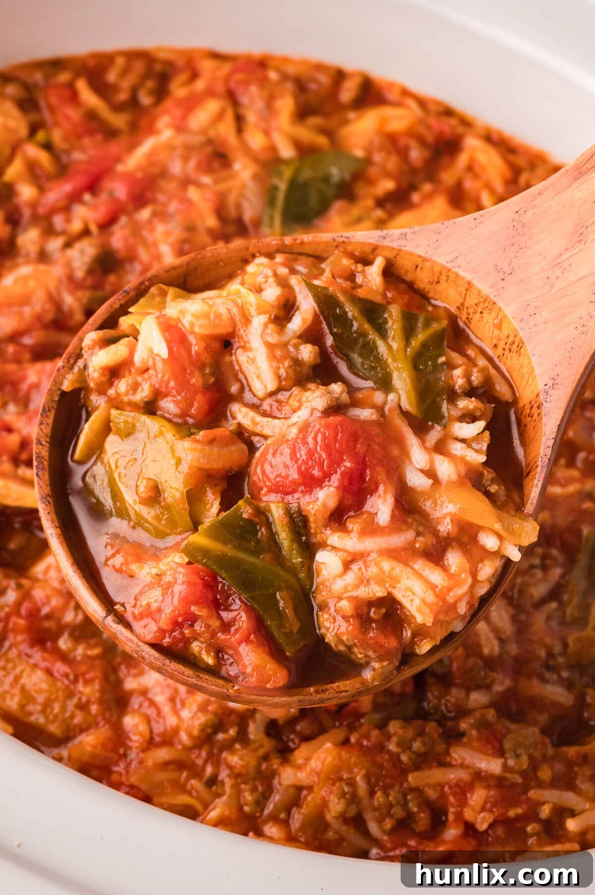 A wooden serving spoon lifting a portion of Cabbage Roll Soup from a bowl, showcasing its rich texture and ingredients.