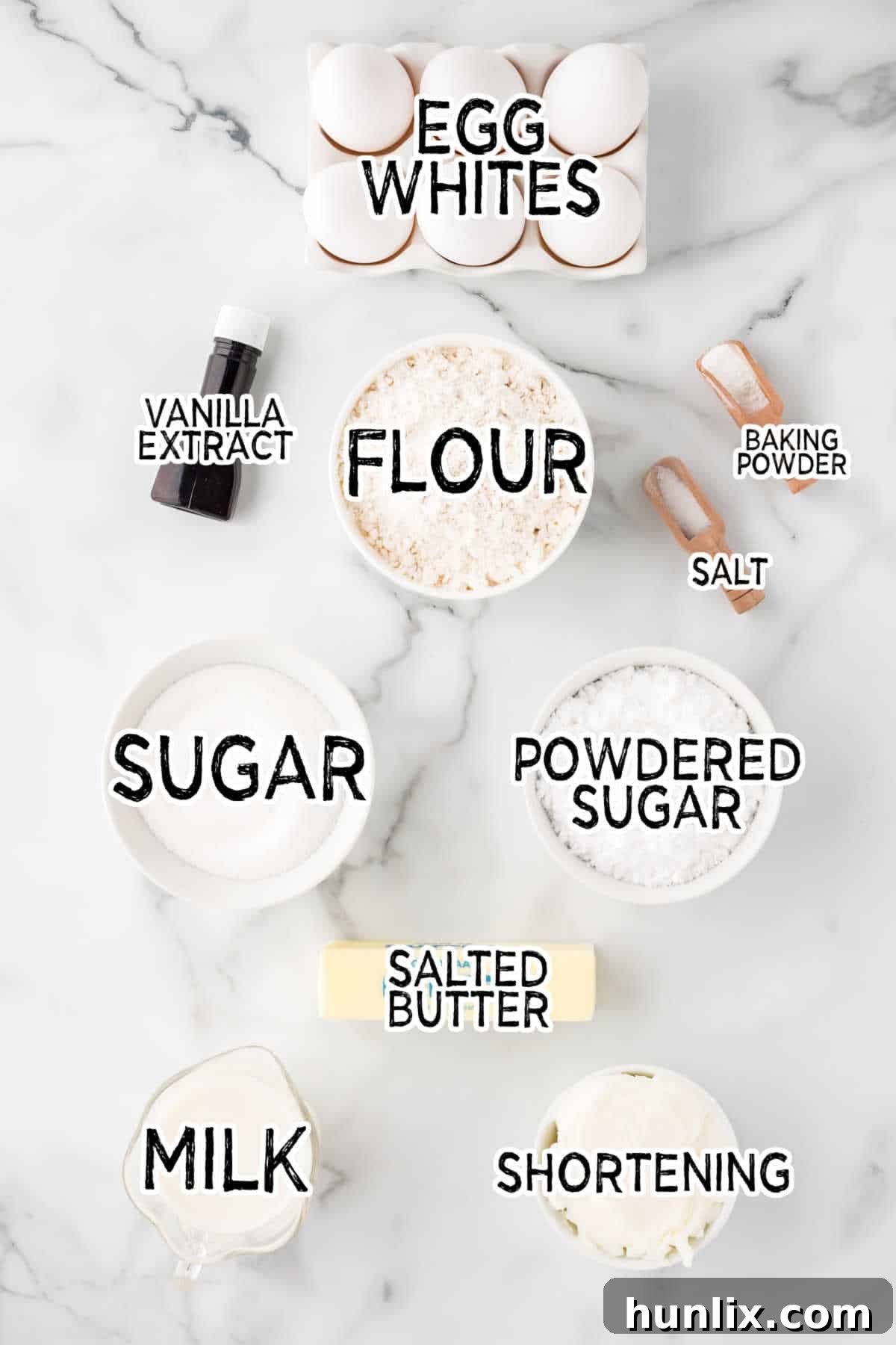 Various baking ingredients, including flour, sugar, eggs, and butter, neatly arranged on a white marble counter, ready for baking.