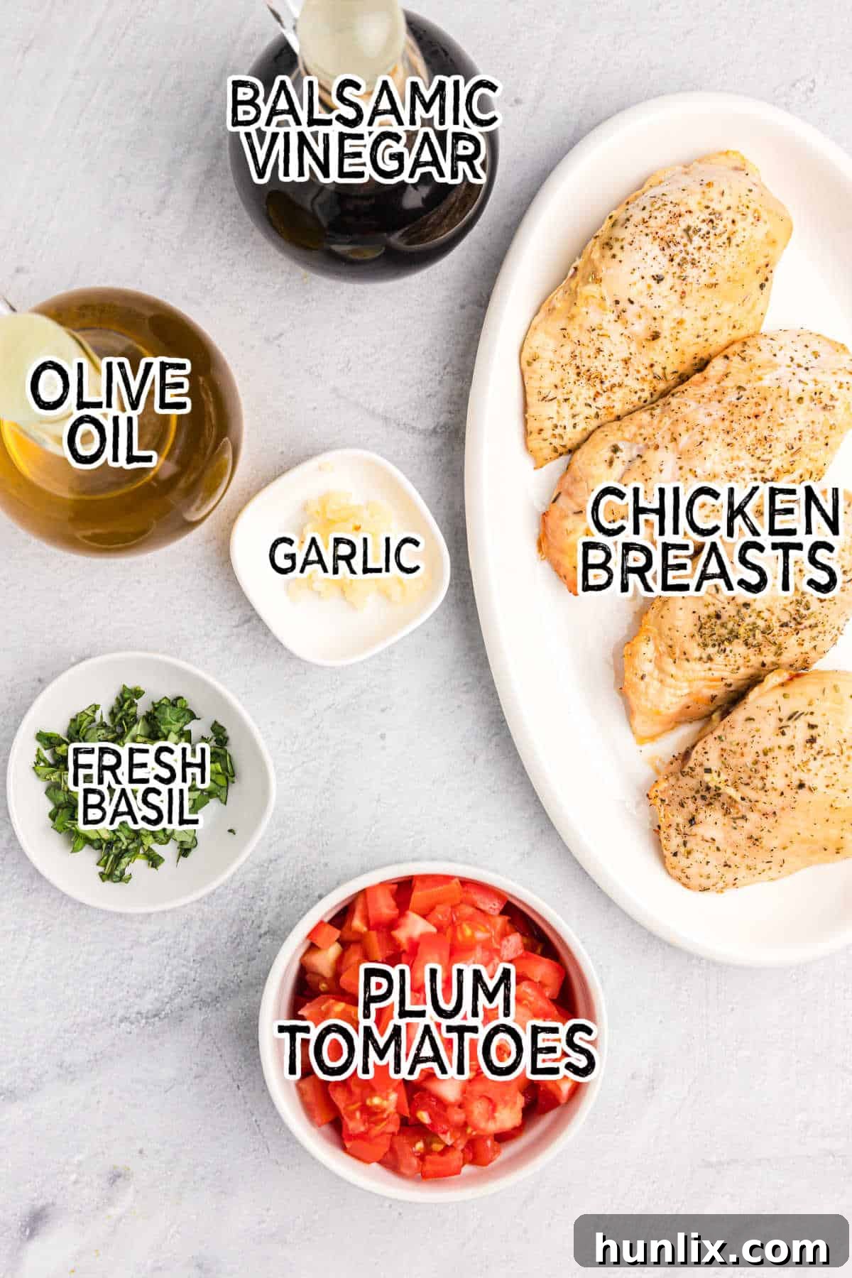 Fresh ingredients for Bruschetta Chicken laid out on a white surface, including tomatoes, basil, garlic, and olive oil.