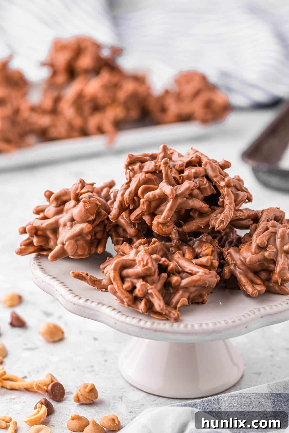 No-Bake Peanut Butter Chocolate Crunch Clusters 2 No-Bake Chocolate Peanut Butter Haystacks on a white pedestal, showcasing their delightful texture and appealing golden-brown color against the dark chocolate.