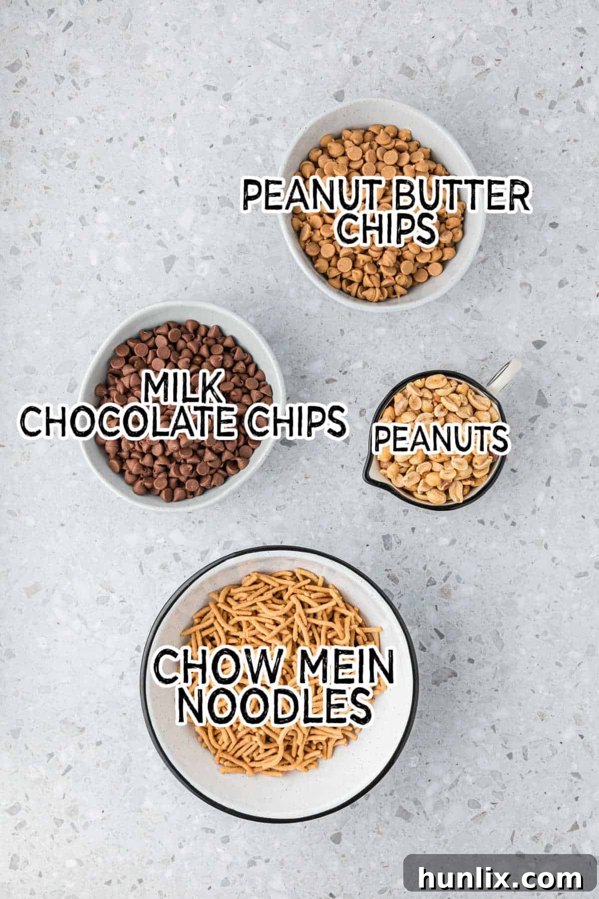 No-Bake Peanut Butter Chocolate Crunch Clusters 3 A vibrant flat lay of all the essential ingredients laid out on a clean grey background, including milk chocolate chips, peanut butter chips, peanuts, and chow mein noodles.
